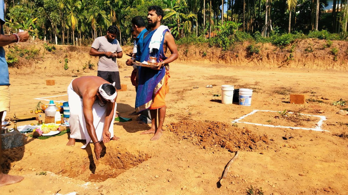 A bhoomi puja on a building plot: an offering placed in the pit while the priest holds the puja plate